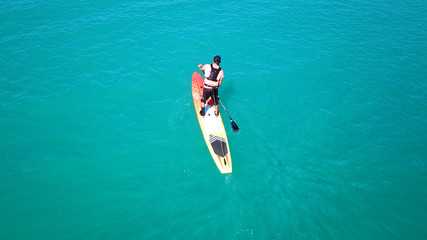 Aerial drone bird's eye view of young man exercising sup board in turquoise tropical clear waters