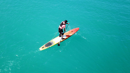 Aerial drone bird's eye view of young man exercising sup board in turquoise tropical clear waters