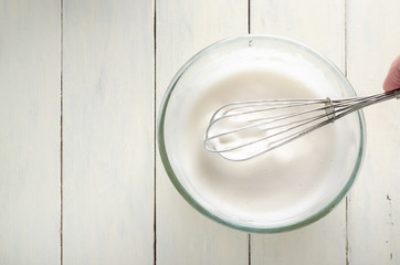 Frothy Aquafaba in Glass Bowl with Whisk From Above on Wood Planked Table