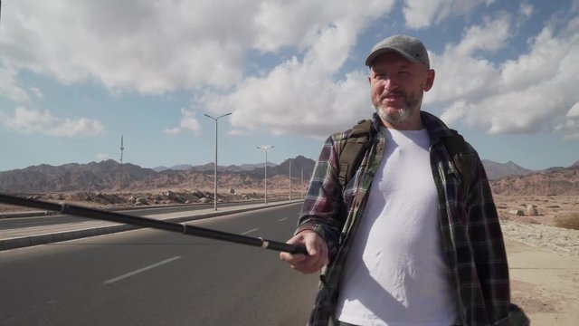 Hand-held shot of walking senior traveler male shooting himself with monopod