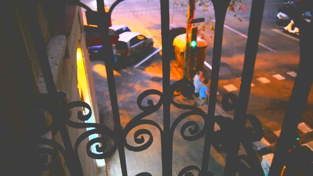 looking to the street through beautiful wrought iron keeper in a first floor balcony in twilight time, in a busy street from the Eixample district in Barcelona, with bus passing and turning