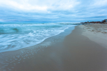 Fototapeta na wymiar sandy beach and tide at sea during blue twilight in cloudy weather on long exposure