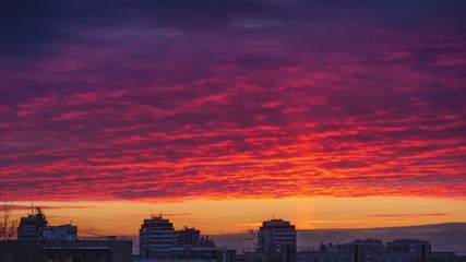 Light pillar atmospheric effect from sunset sun over epic red clouds and dark city skyline. 4K Timelapse.