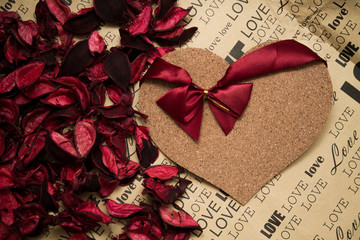 cork heart with red ribbon among red rose petals layed on craft paper
