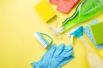 Cleaning concept - cleaning supplies, gloves, bottles on pastel yellow background, copy space