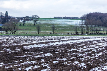 Small strips of snow on plowed fields and meadows. Forest and dairy farm in the background. The...