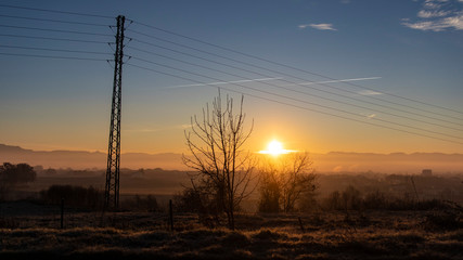 Sun rising on a dark cloudscape with electricity towers on a blue and yellow morning scene on a...