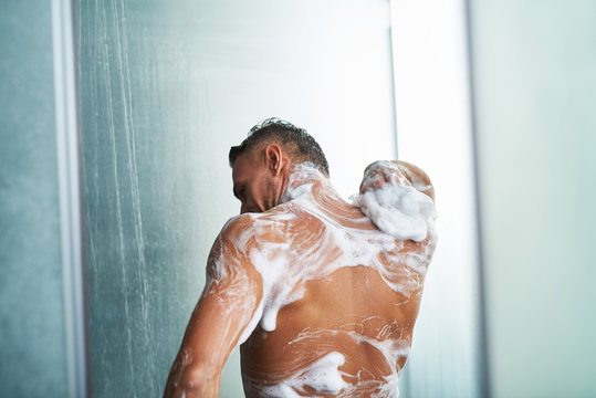 Naked gentleman with foam on his body taking shower at home
