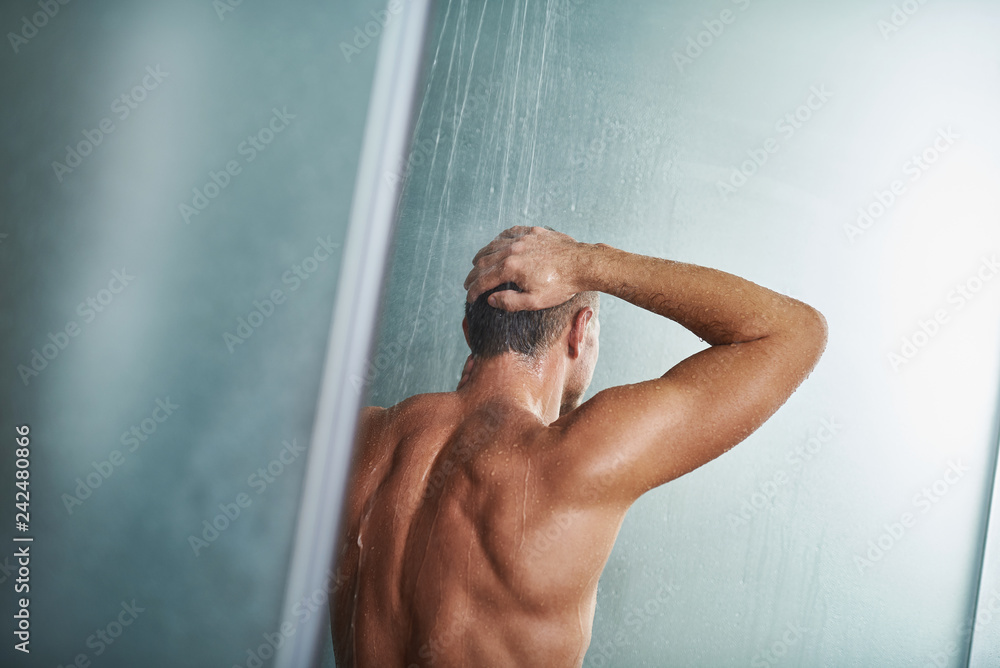 Wall mural young man standing under water drops and keeping hand on head