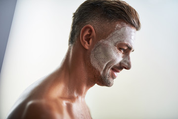 Attractive young man with facial mask standing against white background