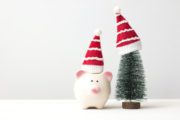 Piggy bank, christmas tree and santa claus hat over white wooden table with copy space. Saving and christmas holiday concept.
