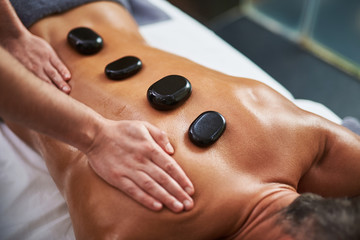 Young man with hot mineral stones on his back receiving spa treatment