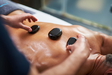 Professional masseur putting hot mineral stones on client back