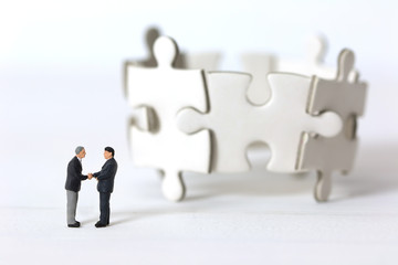 Miniature businessmen shaking hands  on blurred group of jigsaw puzzle background. Concept of partnership successful.