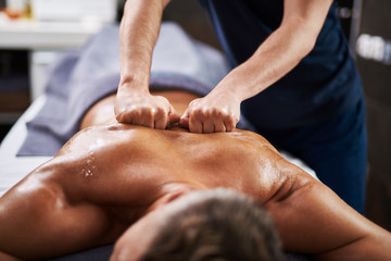 Professional masseur massaging man back at wellness center