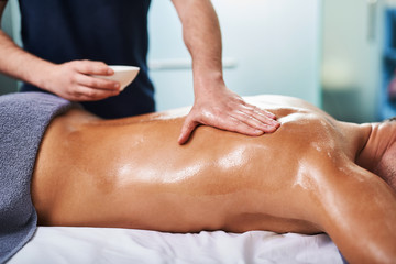 Professional masseur applying massage oil on client back - obrazy, fototapety, plakaty