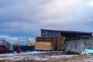 A bit of snow in the meadow. Sawn poles and boards near  the barn. The beginning of winter in...