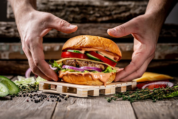 Close-up of the hands holding home made tasty hamburger on wooden vintage table. excess weight set
