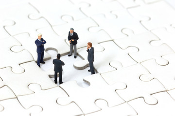 Miniature businessman meeting about lost jigsaw one piece. Business solution and teamwork concept.