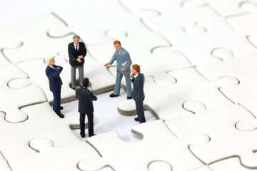 Miniature businessman meeting about lost jigsaw one piece. Business solution and teamwork concept.