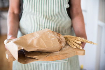 Woman holding cutting board with loaf bread and wheat
