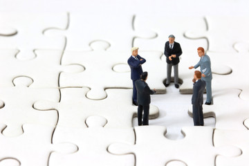 Miniature businessman meeting about lost jigsaw one piece. Business solution and teamwork concept.