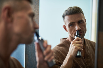 Handsome young man removing hair from nose at home bathroom