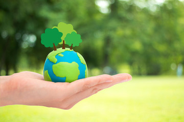 Human hands holding plant trees on the globe, planet or earth over blurred green garden nature background. Ecology concept.