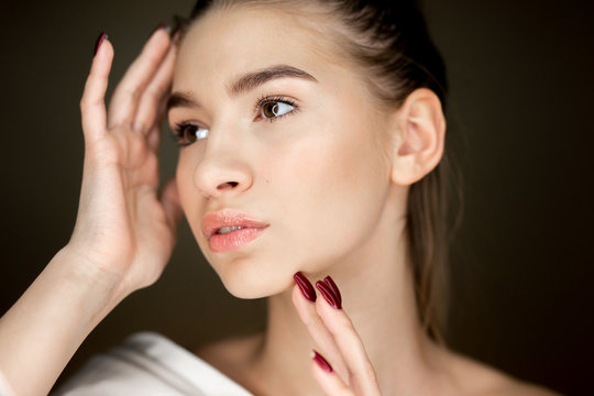 Portrait of young charming girl with natural makeup holding her hands on her face