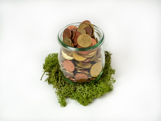 Geldmünzen in einem Glas auf grünen Moos, weißer Hintergrund