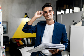 Dark-haired  stylish architect  in glasses dressed in blue checkered jacket and jeans works with...