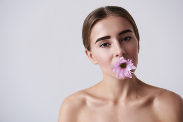 Attractive young woman holding pink flower in mouth
