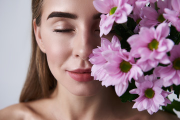 Attractive young woman enjoying aroma of beautiful pink flowers