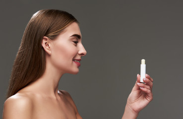 Obraz premium Beautiful young lady with naked shoulders holding hygienic lipstick