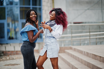 Fototapeta premium Two attractive african american womans posed against modern multistory building.