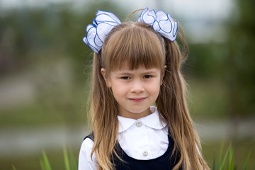 Close-up portrait of cute adorable smiling little first grader girl in school uniform and white...