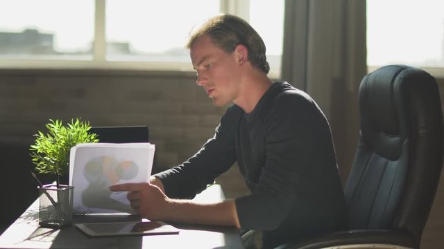 Young blond businessman sit in the modern office, explain work to the members. Financial business chart with diagrams