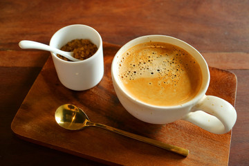Hot coffee with a pot of brown sugar and brass teaspoon on wooden tray