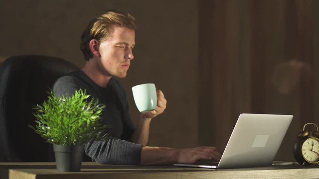 Young blond business man working at notebook at the modern office drinking coffe