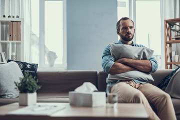 Serious bearded man frowning and hugging a pillow