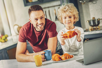 Positive attractive man and boy tasting croissants
