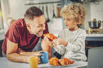 Energetic jolly man and boy degusting croissant