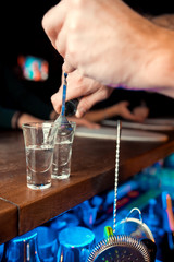 Bartender pouring strong alcoholic drink into small glasses on bar. Red shots at the nightclub. Red alcoholic drink in glasses on bar. Red cocktail at the nightclub. Barman preparing cocktail shooter