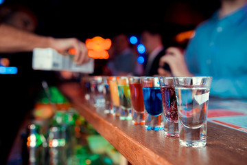 Bartender pouring strong alcoholic drink into small glasses on bar. Red shots at the nightclub. Red alcoholic drink in glasses on bar. Red cocktail at the nightclub. Barman preparing cocktail shooter