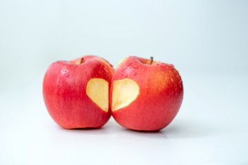 Love of two apples concept with a neatly incised heart in the skin of a ripe red apple on white table
