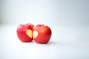 Love of two apples concept with a neatly incised heart in the skin of a ripe red apple on white table