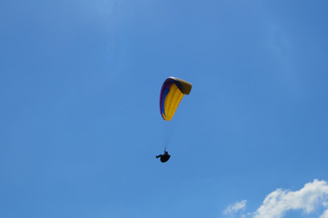 Paraglider flying on colored parachute in blue clear sky at a bright sunny summer day. Active lifestyle, extreme hobbies