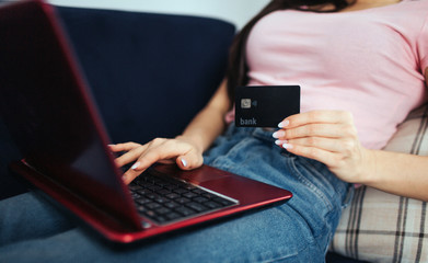 Naklejka premium Cut view of young woman sit on sofa. She type on keyboard. Model hold plastic debit card in hand. She does on-line purchasing.