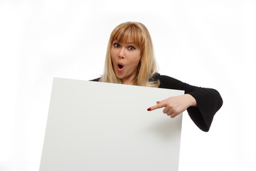 Fototapeta premium Surprised blonde model with a sheet for the text in the hands on a white background. Emotions model. Surprise and invitation. The model shows a finger on the text. A model mouth open. Strong surprise 