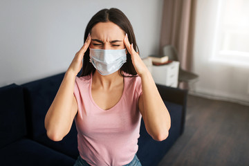 Young woman sit in room. She has terrible headache. Model hold hands on head. She suffer. Young woman hold hands on head.